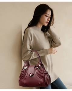 Detail of burgundy textured leather shoulder bag with side pleats and silver metal hardware