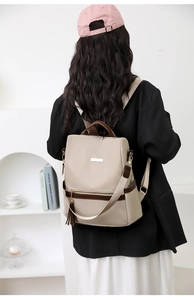 Rear view of model wearing a beige backpack with brown trim and tassel detail