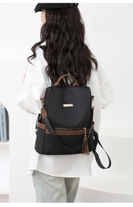 Detail of black nylon backpack with brown leather trim and stylish tassel on back