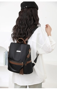 Rear view of black nylon backpack with brown leather trim and tassel detail