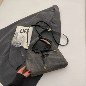 Minimalist dark grey suede shoulder bag with bow detail on a neutral aesthetic background
