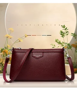 Gros plan détaillé d'un sac bandoulière en cuir rouge foncé avec plaque métallique de logo