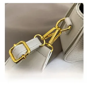 Gros plan du fermoir en métal doré et de la bandoulière large à motifs du sac beige