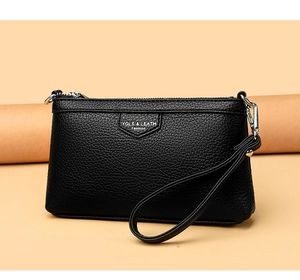 Détail d'une pochette en cuir noir avec motif litchi, fermeture éclair et dragonne argentées
