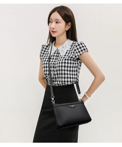Détail du sac bandoulière en cuir grainé noir avec boucles argentées sur un modèle
