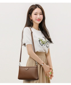Détail du sac bandoulière en cuir marron foncé avec logo en métal et fine bandoulière