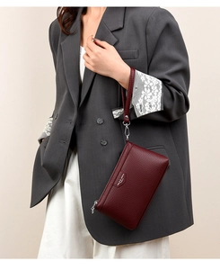 Détail d'une pochette en cuir grainé bordeaux tenue par un mannequin en blazer gris