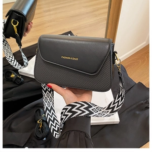 Détail du sac bandoulière noir avec large sangle à motifs et logo doré élégant