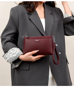Détail de la pochette en cuir rouge foncé avec fermeture éclair argentée portée par un mannequin