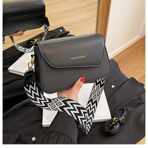 Détail du sac bandoulière noir en cuir texturé avec lettrage doré et large sangle tissée