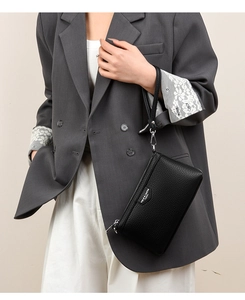 Détail de la pochette enveloppe noire en cuir grainé avec logo argenté sur veste grise