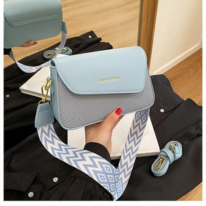 Détail du sac bandoulière bleu clair avec sangle tissée et lettrage doré élégant