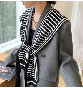 Detail of a black and white striped knitted shawl draped over a grey double-breasted blazer