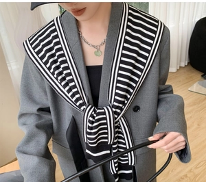 Detail of grey blazer styled with a black and white striped knit shawl and chic heart necklace