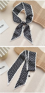 Détail d'un foulard étroit noir à petites fleurs blanches posé sur un plateau en bois chic