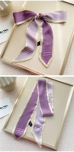 Détail d'un foulard étroit en soie bicolore violette noué en nœud sur un plateau doré