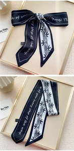 Détail d'un foulard étroit en soie avec texte cursif et motifs géométriques noirs et blancs