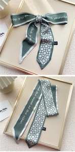 Détail d'un foulard twilly vert foncé avec écriture élégante et motifs géométriques