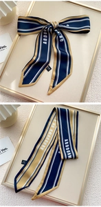 Détail d'un foulard étroit en soie pure avec motifs de lettres bleu marine et dorées