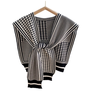 Classic black and white houndstooth knit shawl with striped edges on a wooden hanger