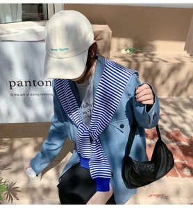 Detail shot of striped knitted shawl draped over a light blue blazer with a casual hat