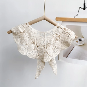 Detailed view of cream hollow leaf crochet shawl with tie closure on a wooden hanger