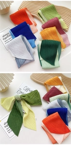 Macro detail of pleated long silk scarves in vibrant orange, emerald, and royal blue
