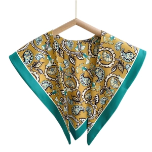 Ginger yellow paisley triangular shawl scarf with green borders hanging on a wooden hanger