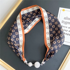 Close-up of silk scarf necklace with monogram print and magnetic rhinestone balls