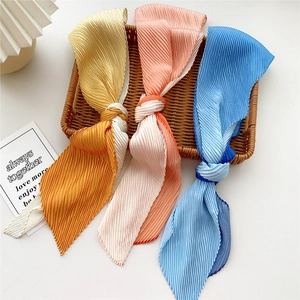 Three gradient pleated scarves in yellow, pink and blue displayed in a woven basket