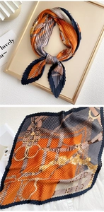 Macro detail of pleated silk scarf with luxury chain print in orange and navy blue