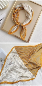 Detail of pleated silk scarf with yellow stripes and floral patterns in a gold frame