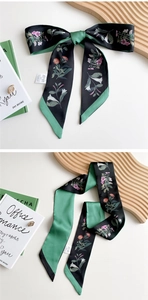 Macro shot of long floral twilly scarf with black and green flower pattern and care label