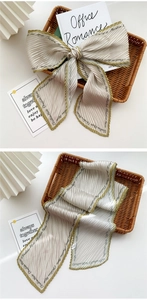 Detail of pleated silk scarf with green edges and elegant brand lettering in a chic bow