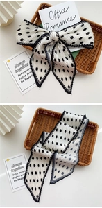 Detail of black polka dot pleated silk scarf tied in a bow on a woven tray background