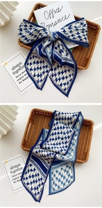 Detail of pleated long silk scarf with blue and white houndstooth pattern on a white desk