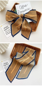 Detailed view of yellow accordion-pleated scarf with navy blue stripes and bow styling