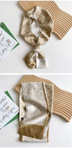 Detail of long silk scarf with golden geometric patterns on a white background