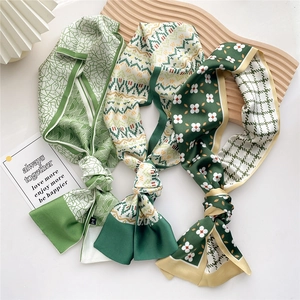 Three green skinny silk scarves with geometric and floral prints on a wooden tray