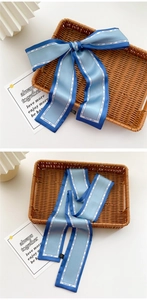 Detailed view of a slim blue silk scarf with fashion text and woven tray decoration