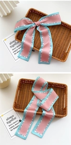 Detailed view of a pink and blue narrow silk scarf tied in a bow on a woven tray
