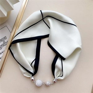 Detail of white silk scarf with black piping and shimmering rhinestone ball buckles