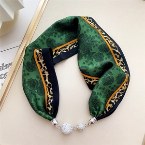 Detail of a green silk scarf with floral patterns and a sparkling rhinestone metal buckle