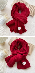 Detailed waffle knit texture of a red wool scarf with handmade label and ribbed edge
