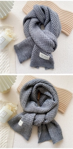 Close-up of grey knitted scarf showing thick wave texture and handmade fabric label