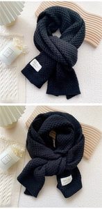 Close-up of black chunky knit scarf with white woven label showing handmade texture