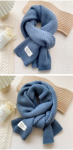 Detail of chunky knit scarf in dusty blue featuring a minimalist white woven label