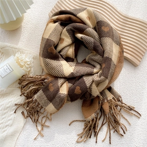 Détail d'une écharpe d'hiver avec motif à carreaux cœur marron et pompons