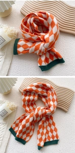 Gros plan d'une écharpe en maille à losanges orange avec bords côtelés verts et texture chaude