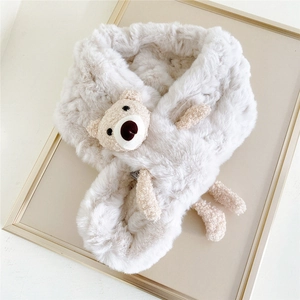 Detailed view of white faux fur scarf with cute plush bear ornament on soft fabric